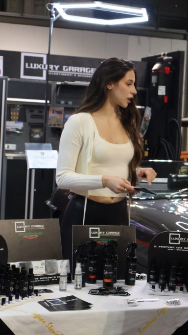 A woman at a trade show stands beside a table of automotive products.