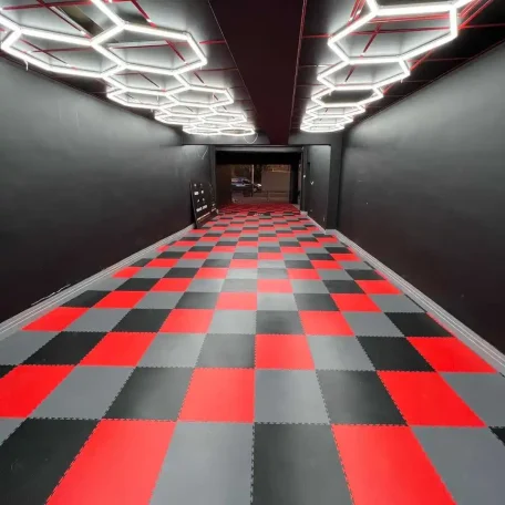 Corridor with a checkered black, red, and gray floor, illuminated by geometric overhead lights.