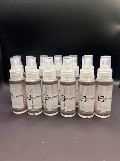 Righe di bottiglie spray trasparenti con etichette chiare su sfondo scuro.