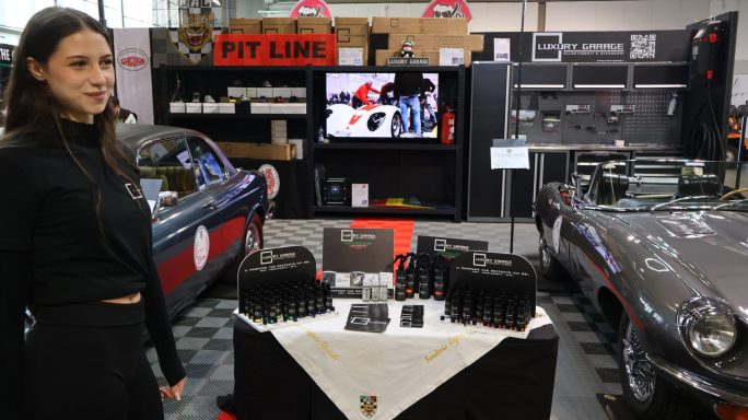 Stand with products on display, vintage cars in the background, and a screen showing a race.