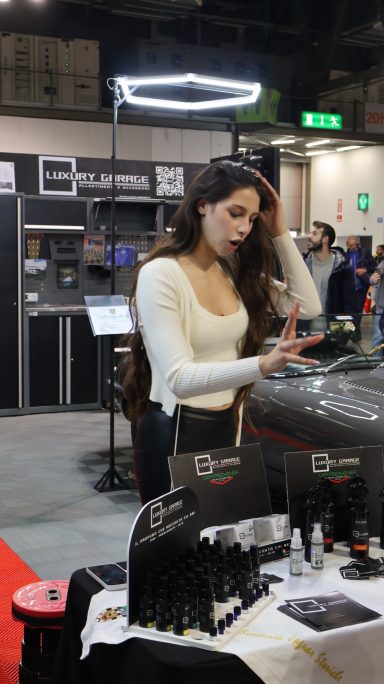 Una donna con i capelli lunghi e mossi interagisce con un prodotto su un banco in fiera.